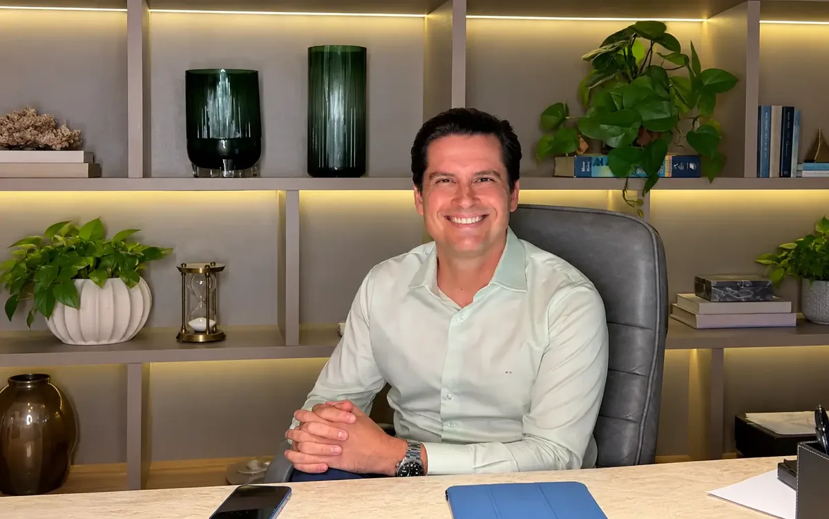 Dr. Manoel Hollanda sorrindo, sentado à mesa de atendimento
